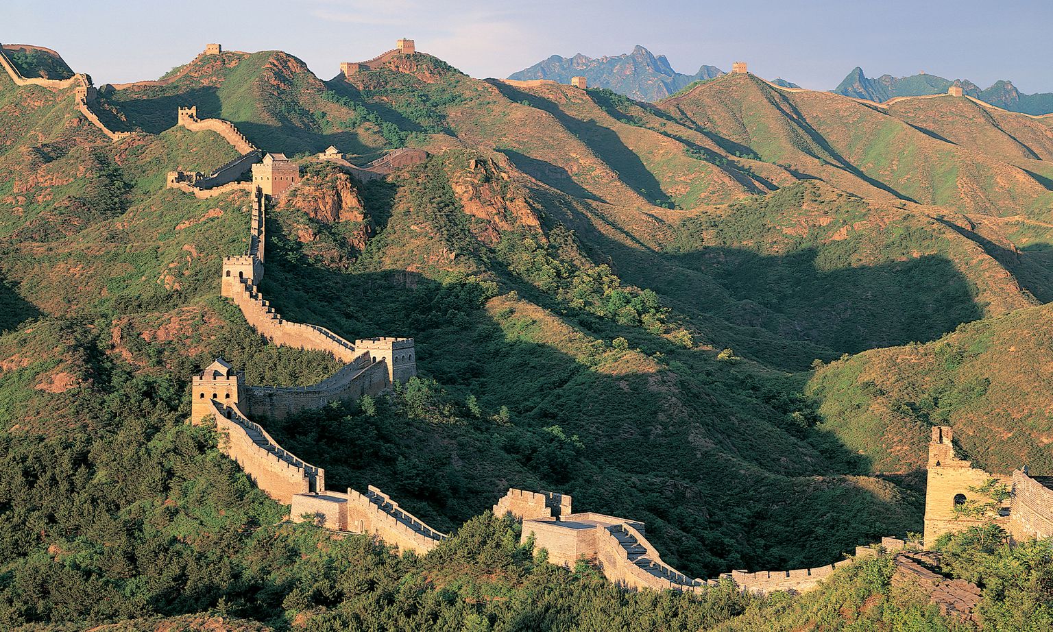 A section of the Great Wall of China and the surrounding mountains at sunset