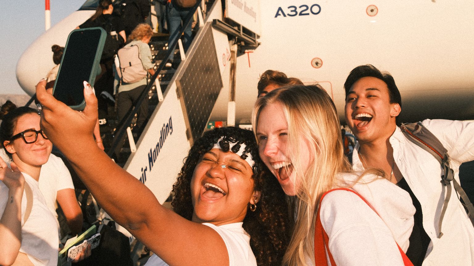 A group of travelers taking a selfie with a plane in the background.