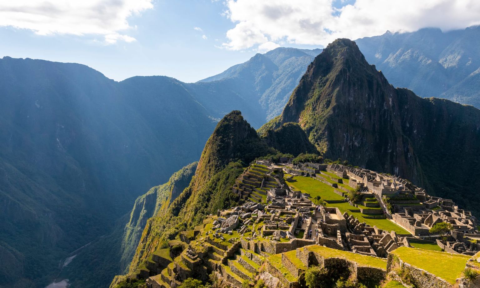 Scenic view of Machu Picchu ruins with grassy terraces, steep mountains, and a clear blue sky in the background.