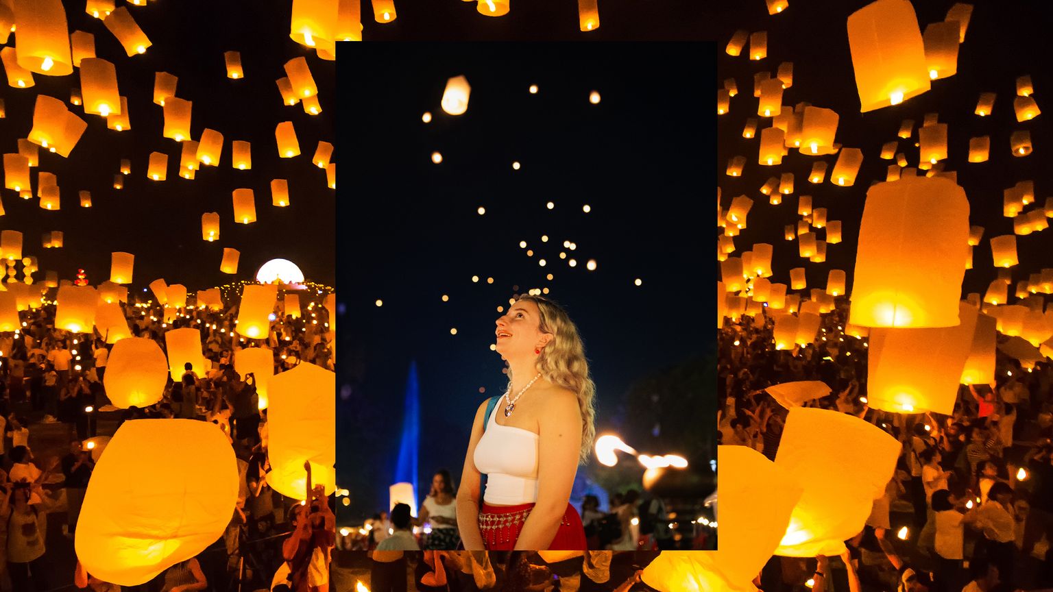 A woman looking up at the lit up floating lanterns in the air.