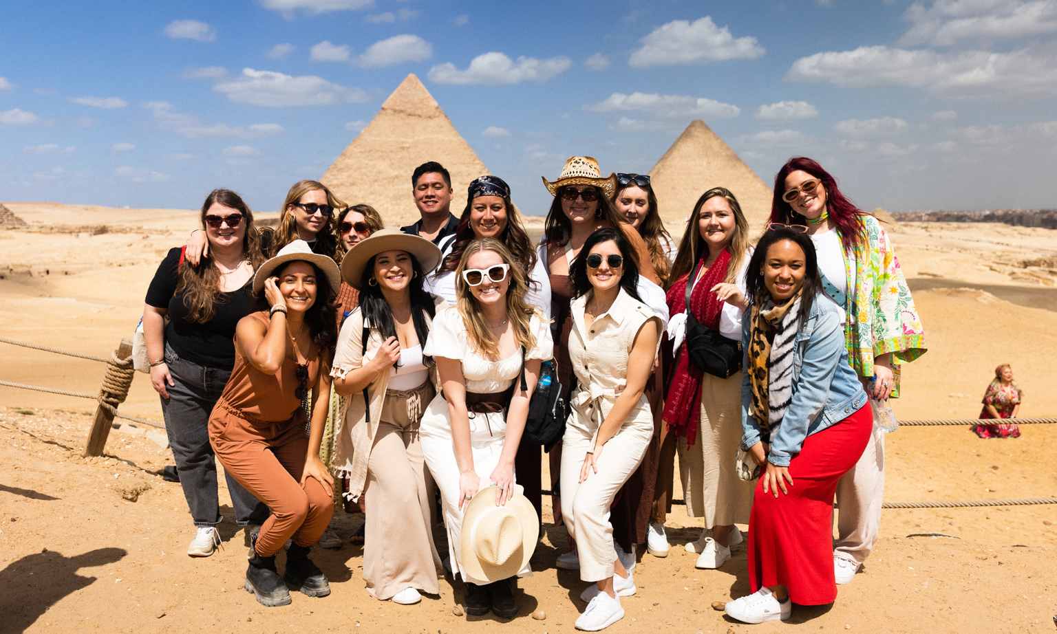 Group of people posing in front of the pyramids in Egypt, under a clear blue sky.