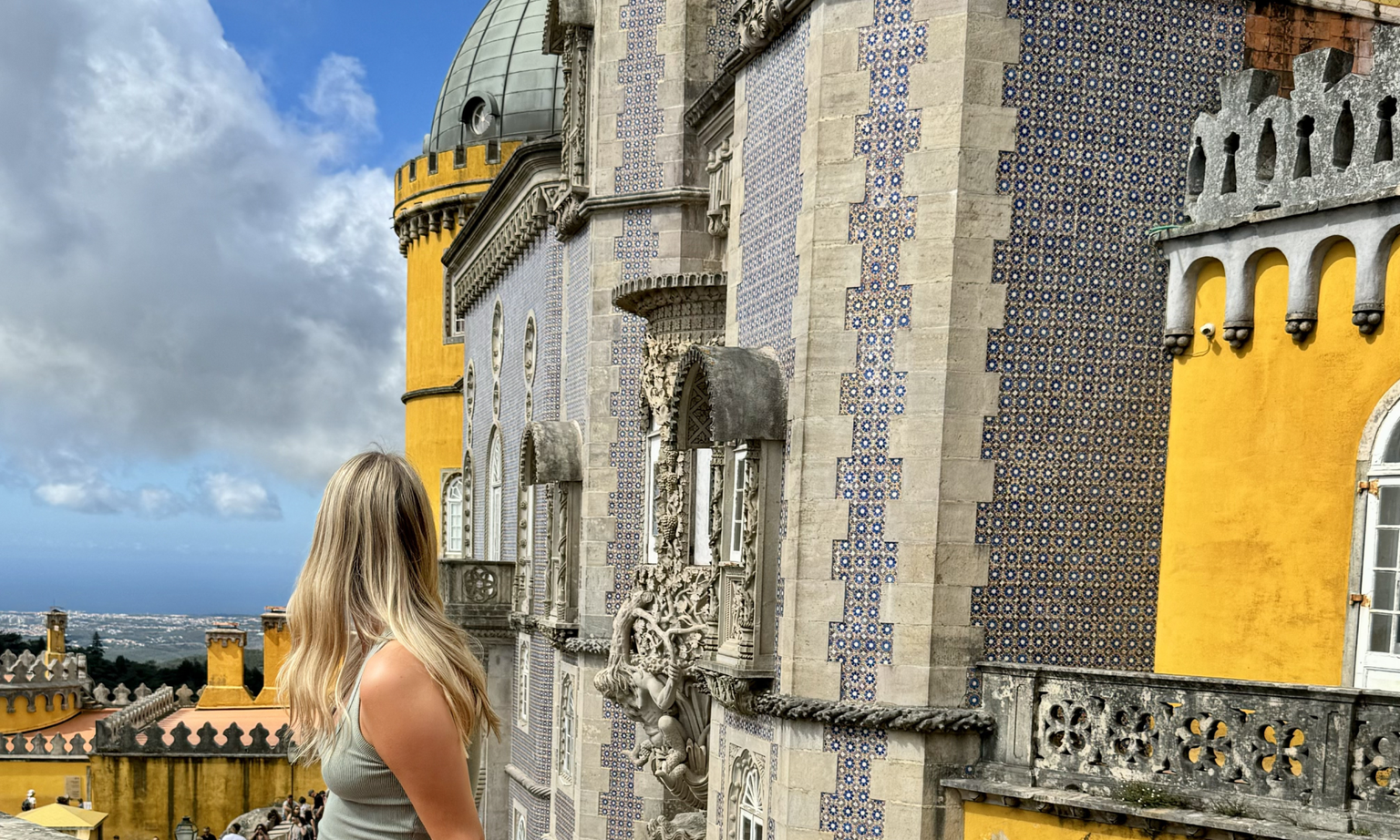A woman looking away from the camera at a bright yellow castle covered in blue Portuguese tiles