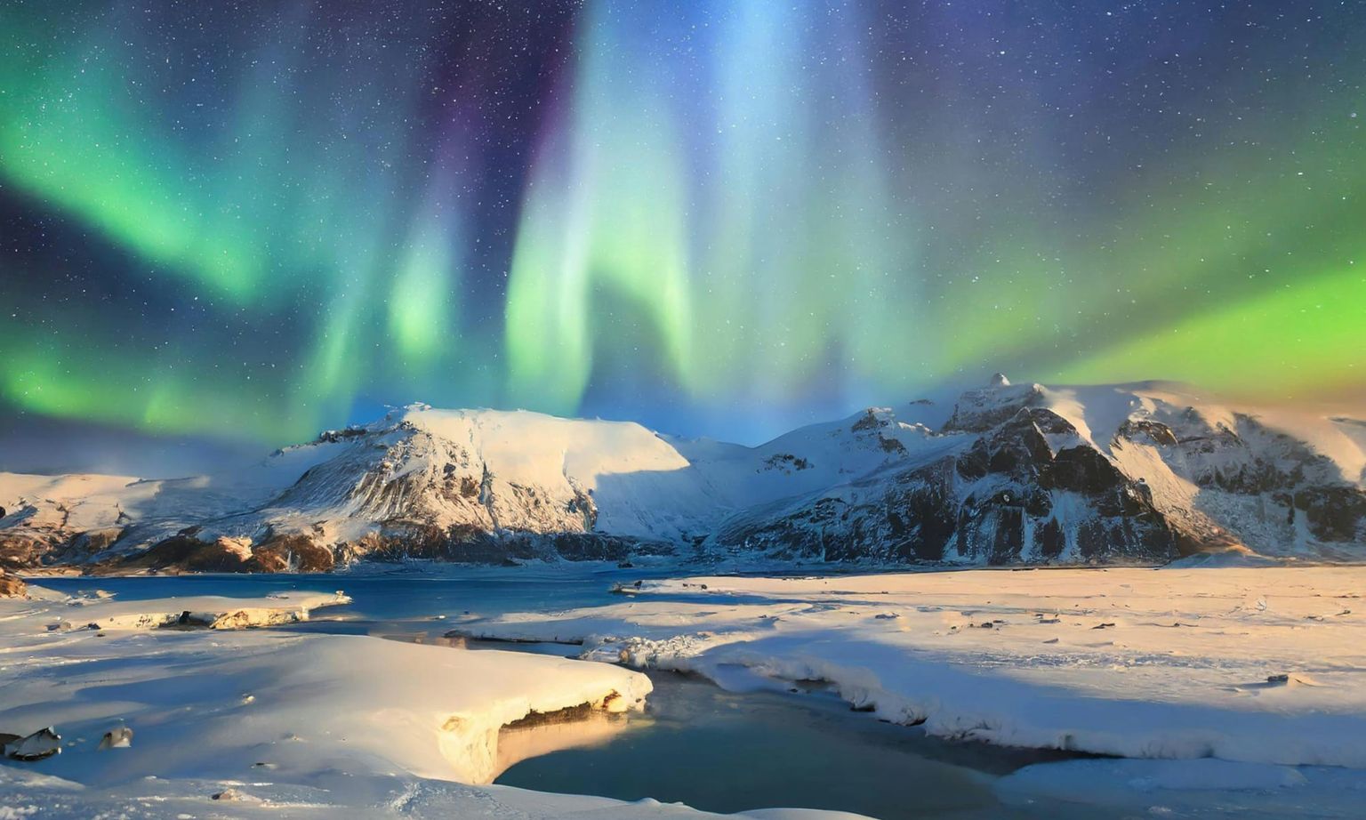 Aurora borealis illuminates a snowy landscape with mountains and a frozen river under a starry night sky.