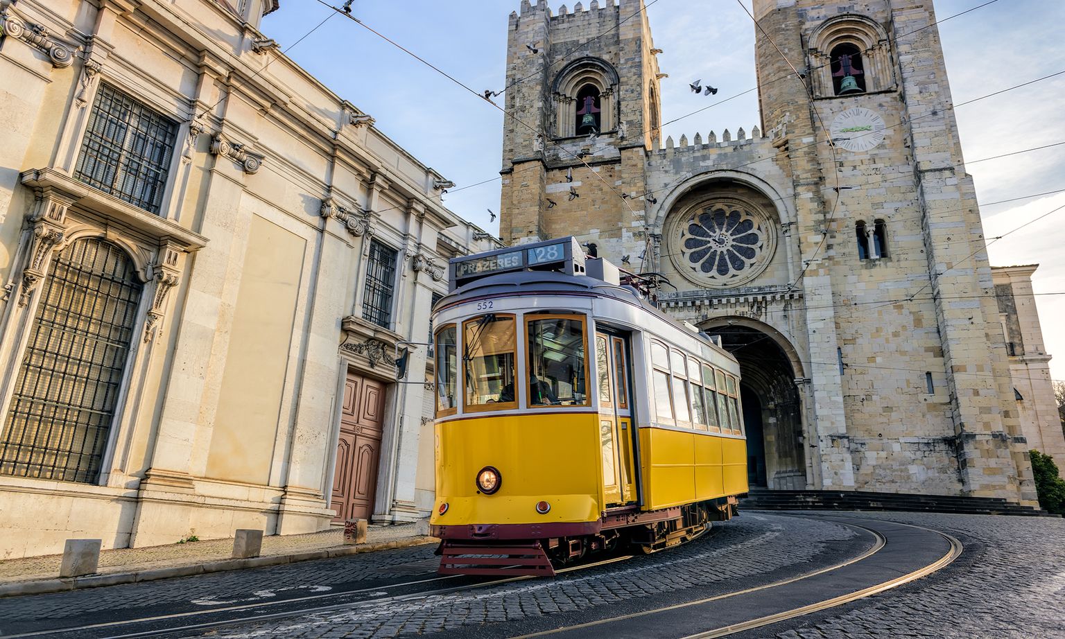 The famous yellow 28 tram moving down a hill in front of a large stone cathedral