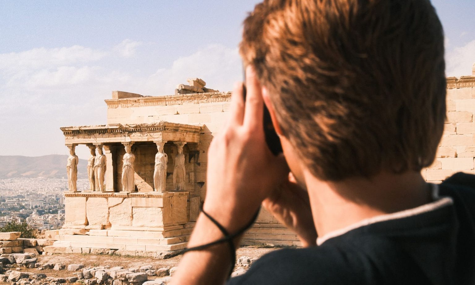 Person taking a photo of the Erechtheion with its iconic Caryatids under a clear sky, situated on the Acropolis in Athens.