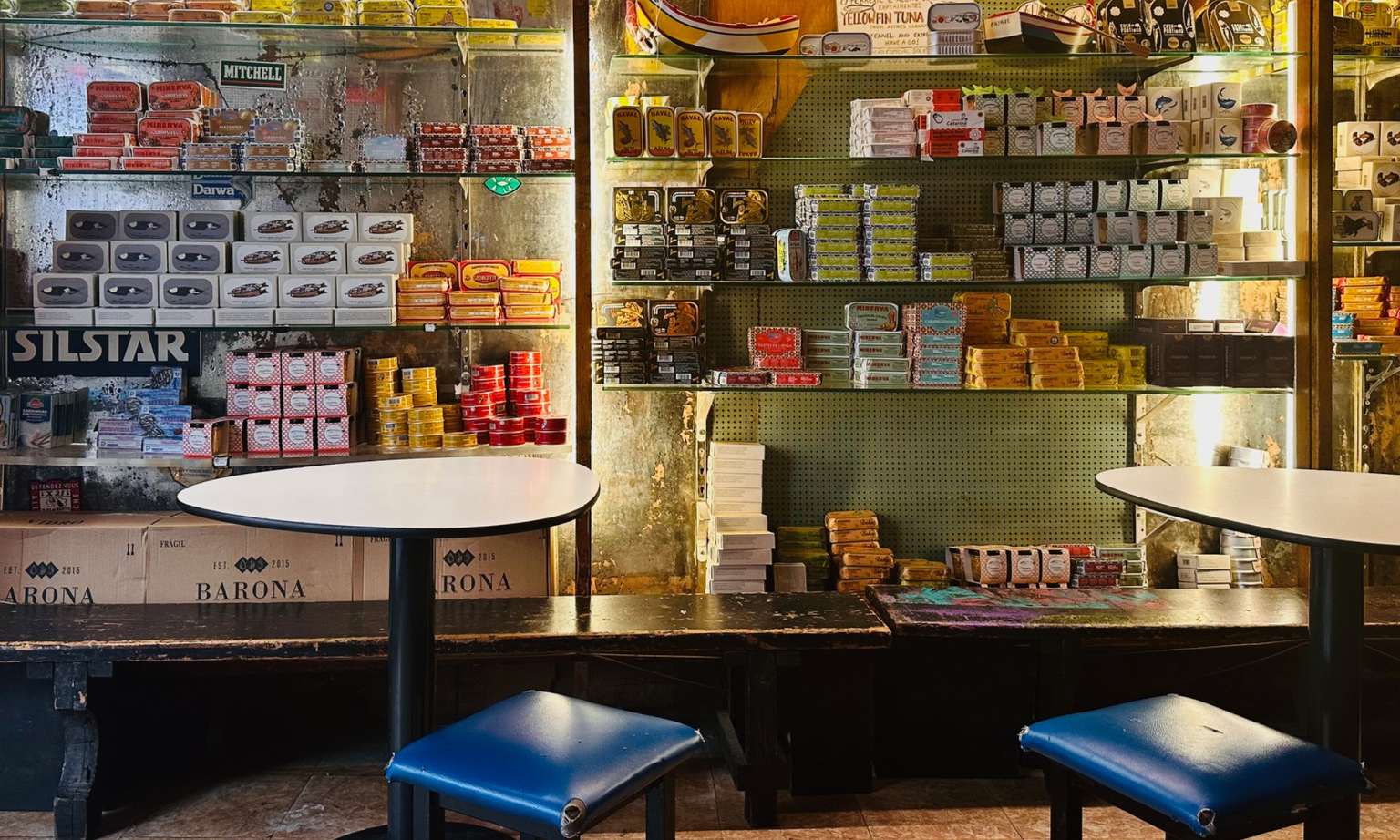 A cozy store interior with shelves stocked with various colorful products, two round tables, and blue chairs in the foreground.