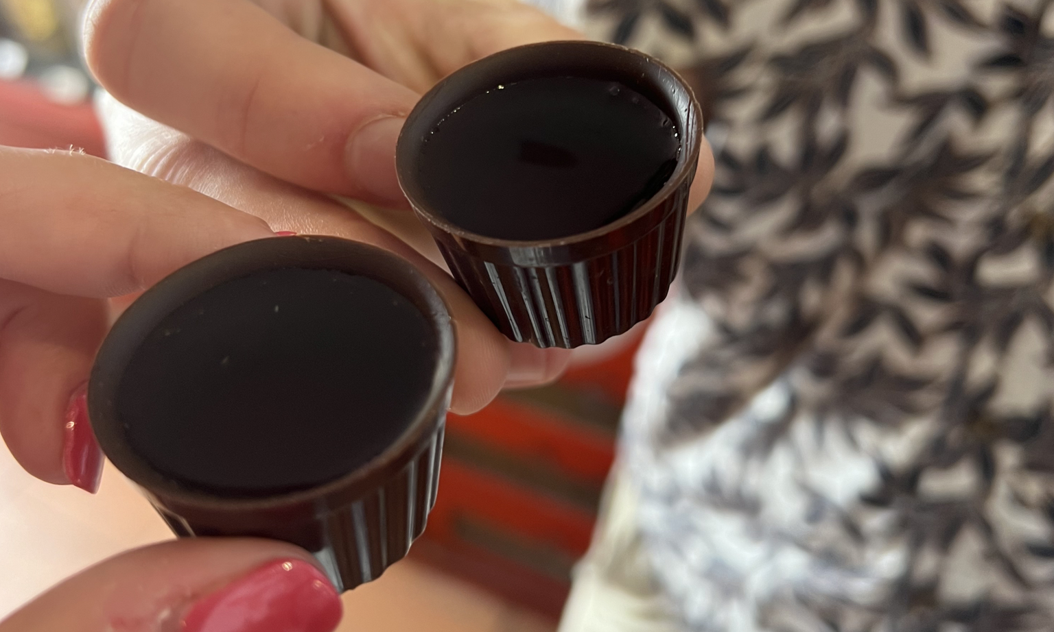 Two hands holding tiny chocolate cups filled with traditional Portuguese cherry liqueur