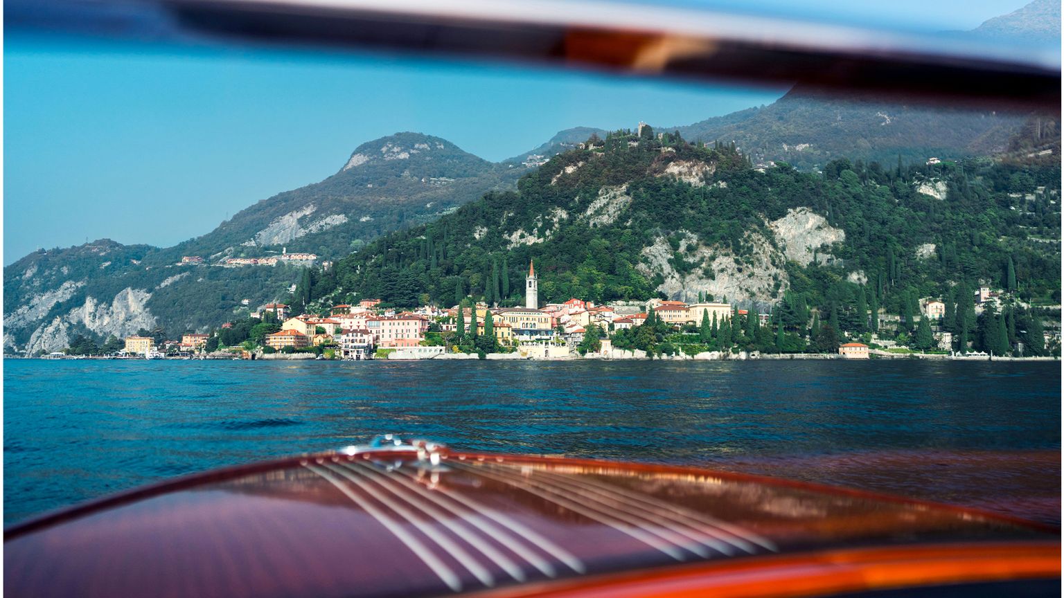 A town and mountains on the edge of Lake Como viewed through the windshield of a vintage boat