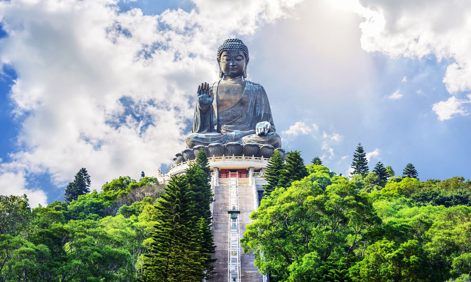 The huge Tian Tan Buddha perch at the top of a staircase surrounded by trees on Lantau Island