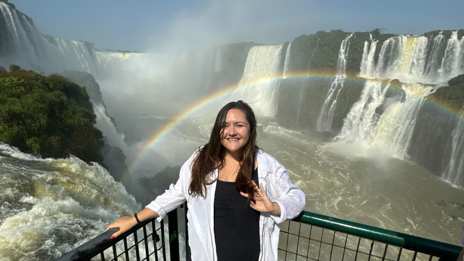 A woman smiling in front of an enormous waterfall and rainbow