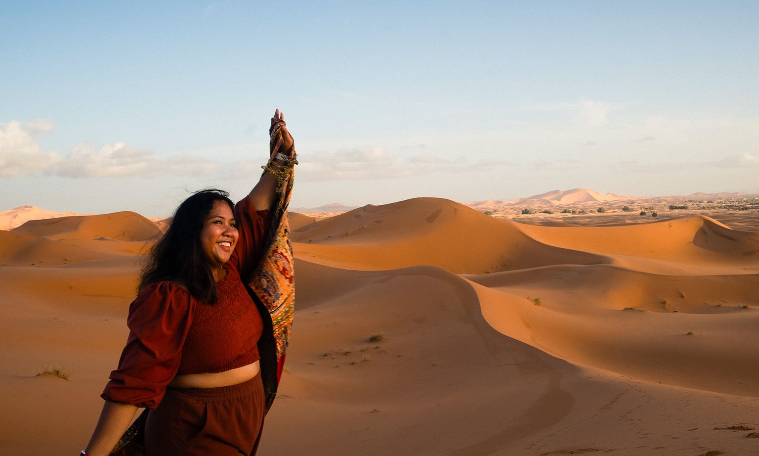 A woman smiling in the sand dunes of the Sahara Desert in Morocco