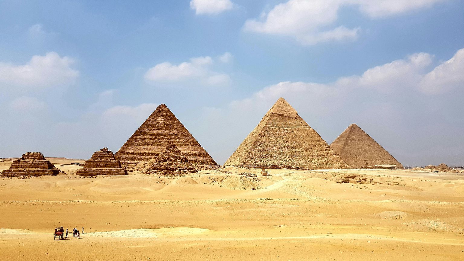 A carriage with people at the base of the Great Pyramids of Egypt.