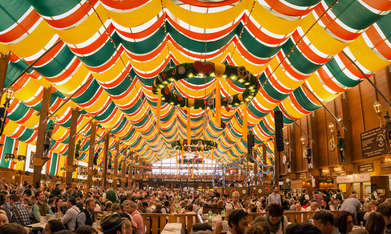 Inside the Schützen-Festzelt Oktoberfest tent with yellow, red, and green ribbons hanging from the ceiling and people sitting at tables.