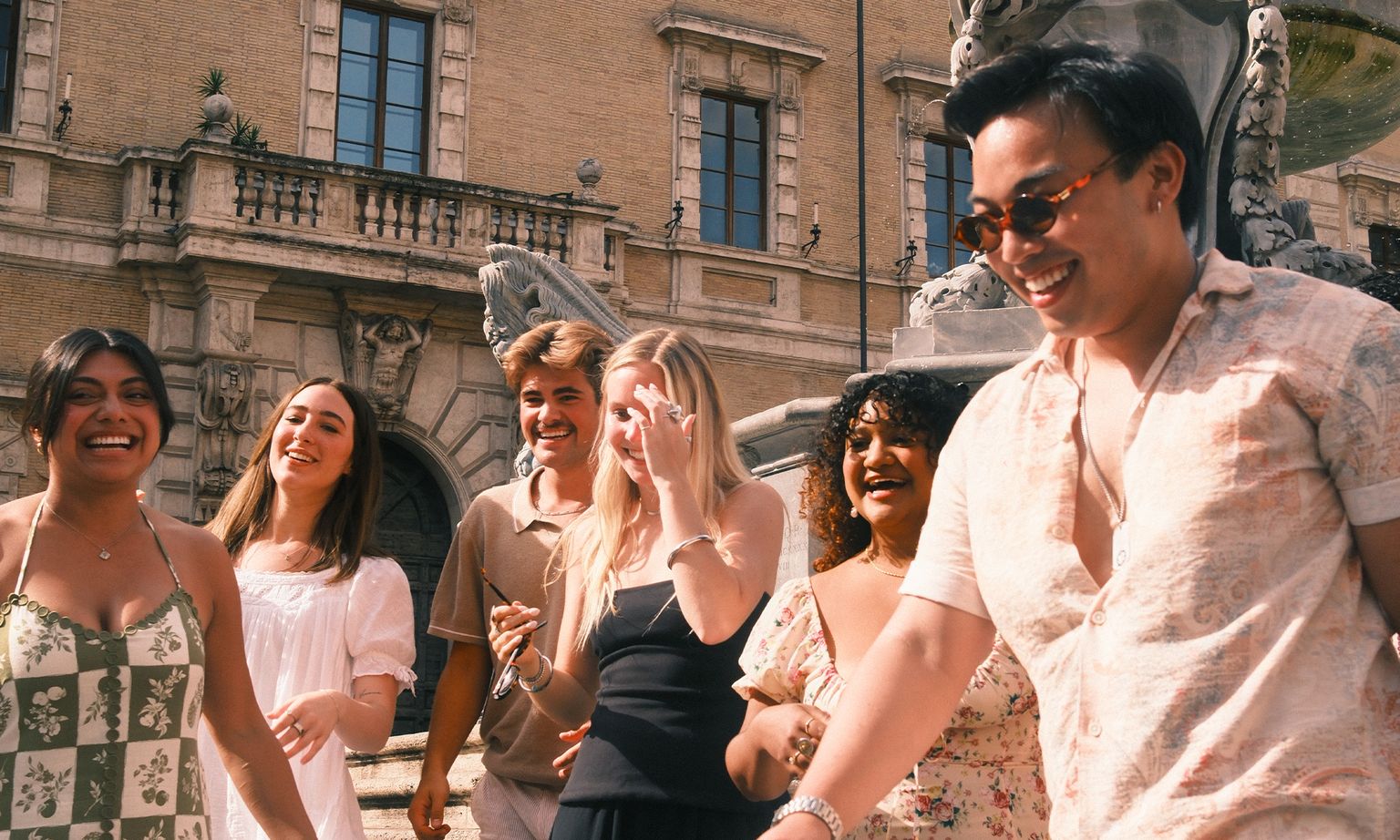 A group of six people laughing and walking together in front of an ornate historic building.