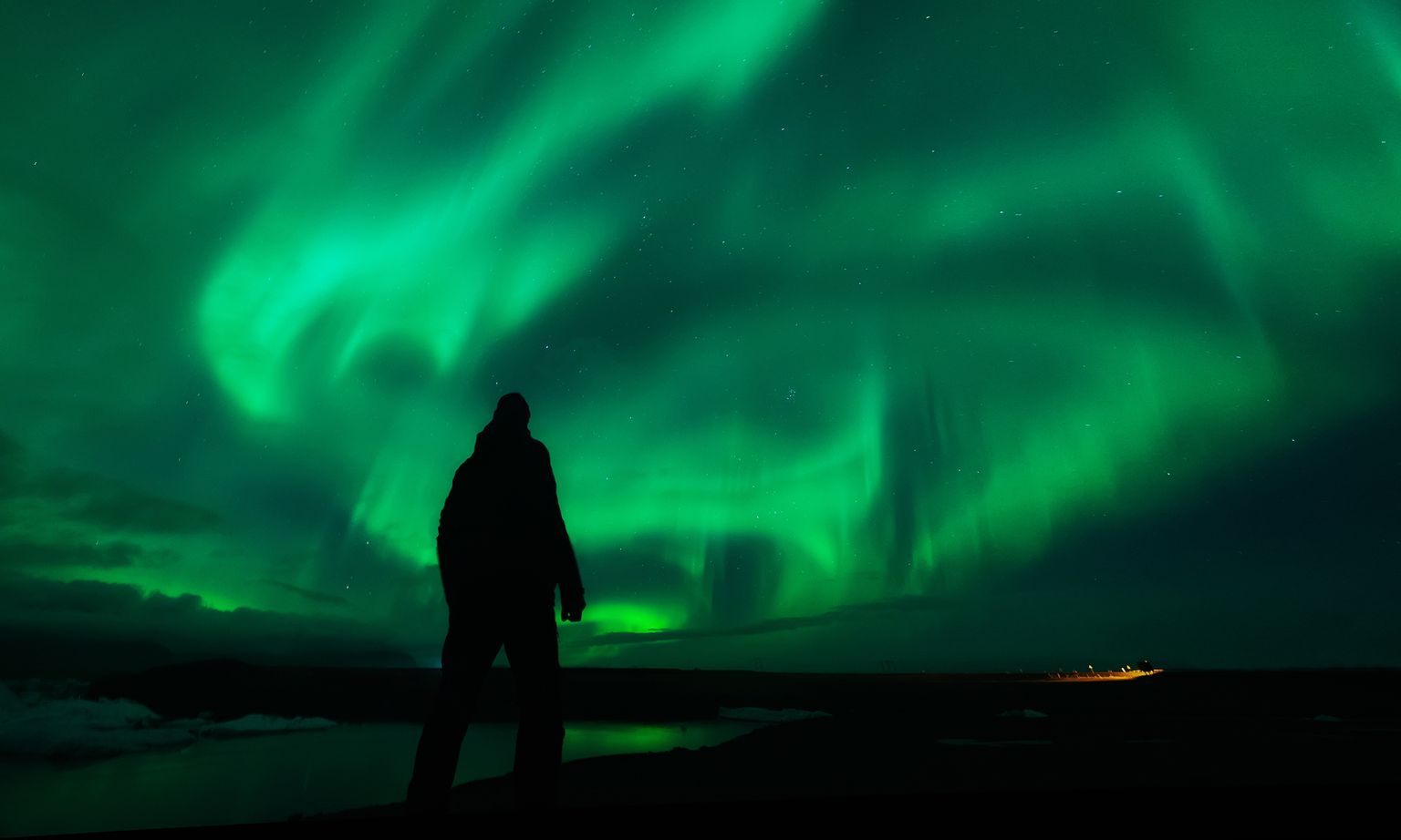 Silhouette of a person standing under vibrant green northern lights in a dark, starry sky.