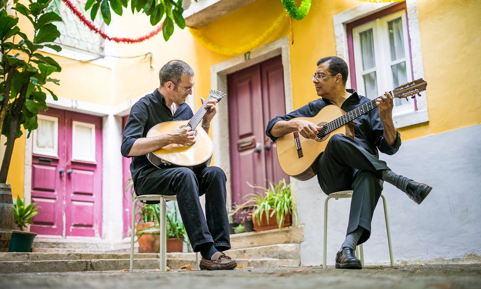 Two Fado musicians playing guitars on the street in front of colorful building in Lisbon, Portugal
