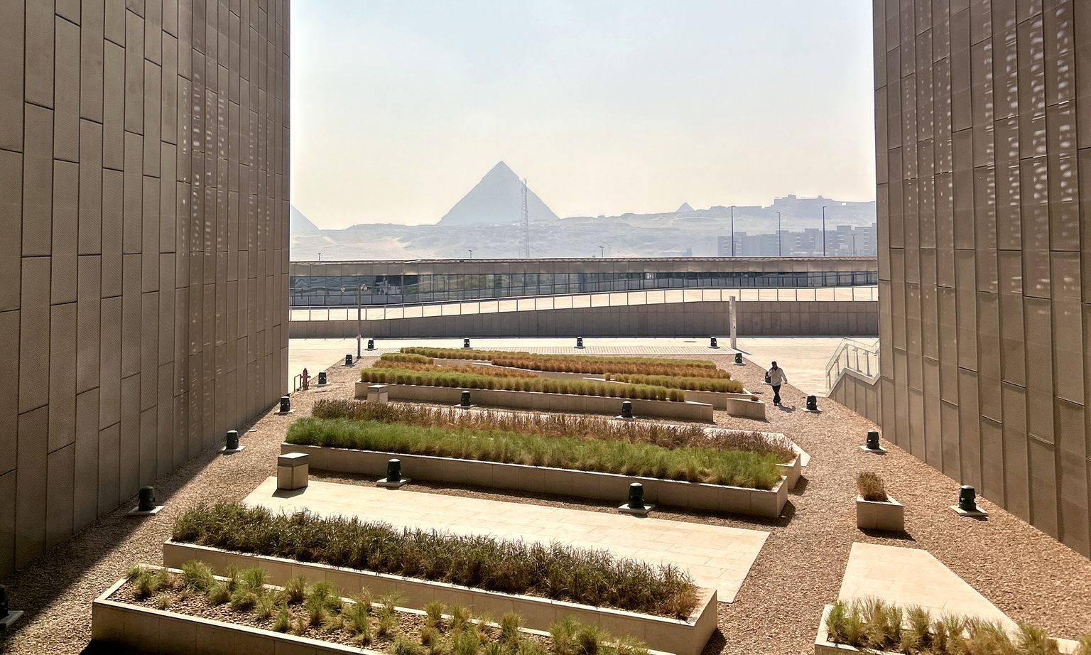 Raised beds of deserts plants set between two tall walls with the Pyramids of Giza in the background at the Grand Egyptian Museum in Cairo, Egypt