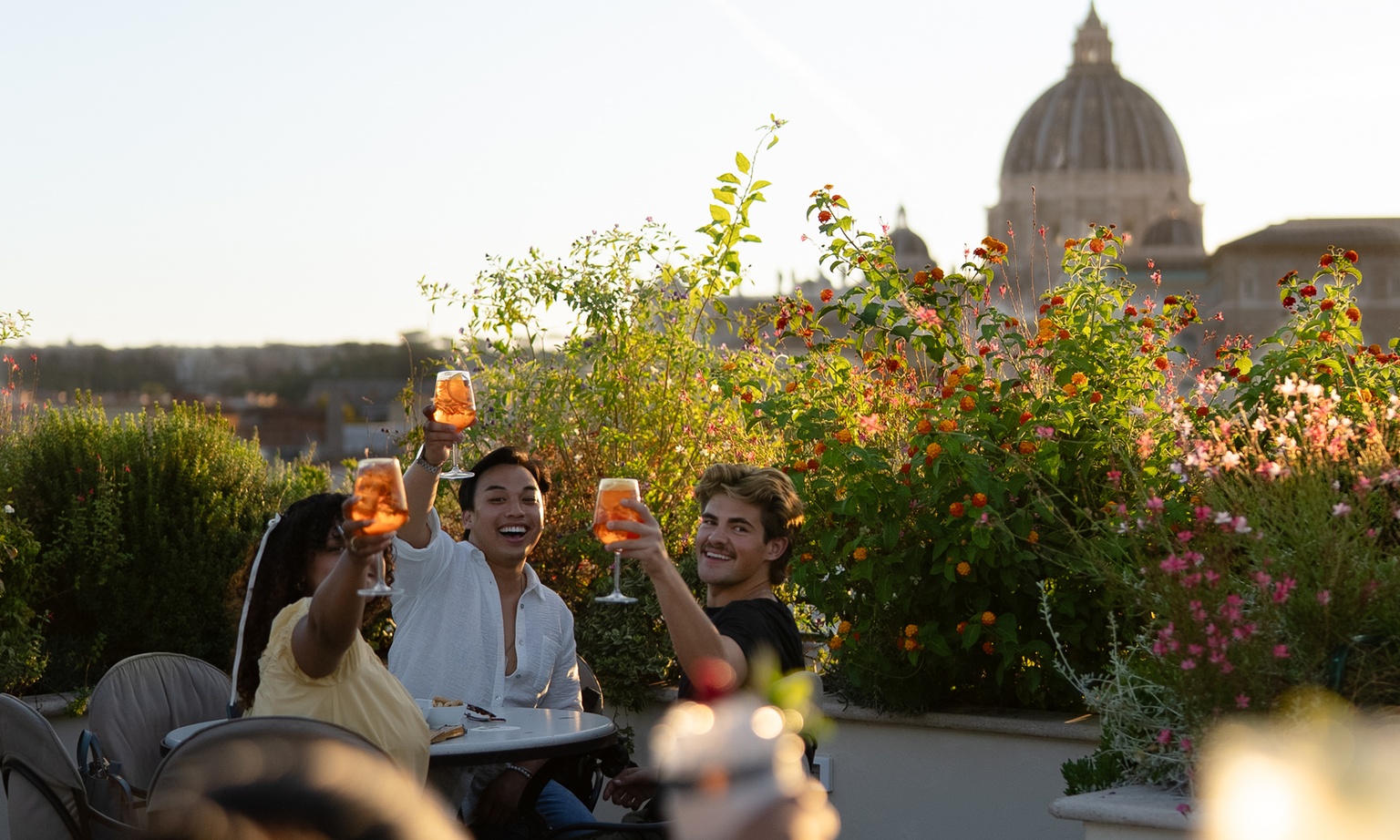 Two men and one woman sipping spritz with a view of St. Peter's Basilica in Rome, Italy