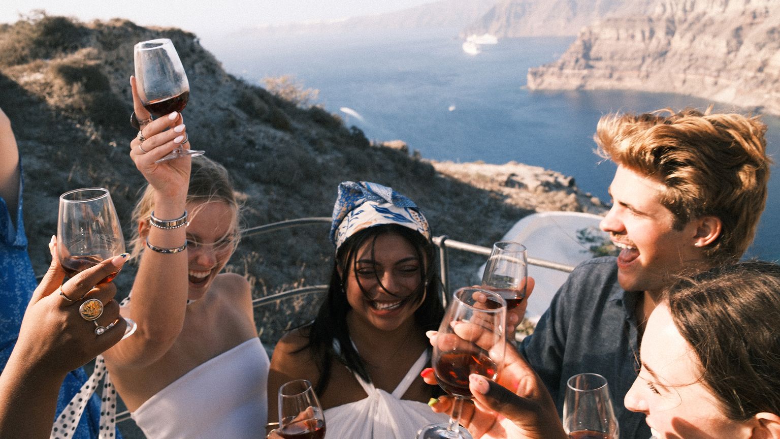 A group of travelers raising their wine glasses while overlooking an ocean cliffside.
