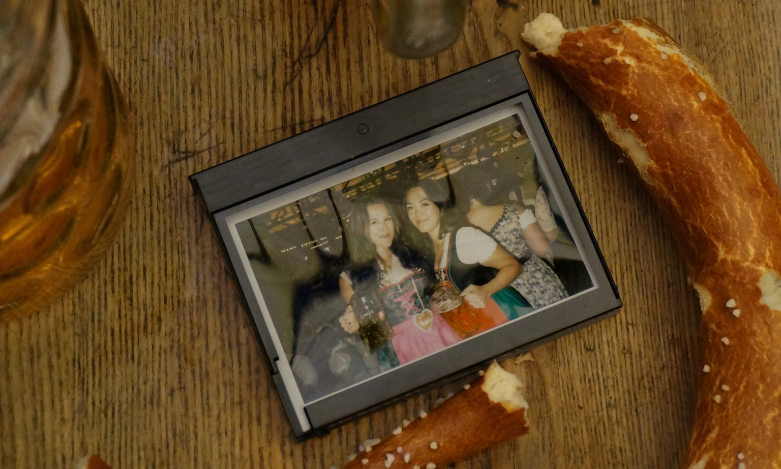 A framed photo of two people in traditional attire on a wooden table surrounded by a broken pretzel and a glass.