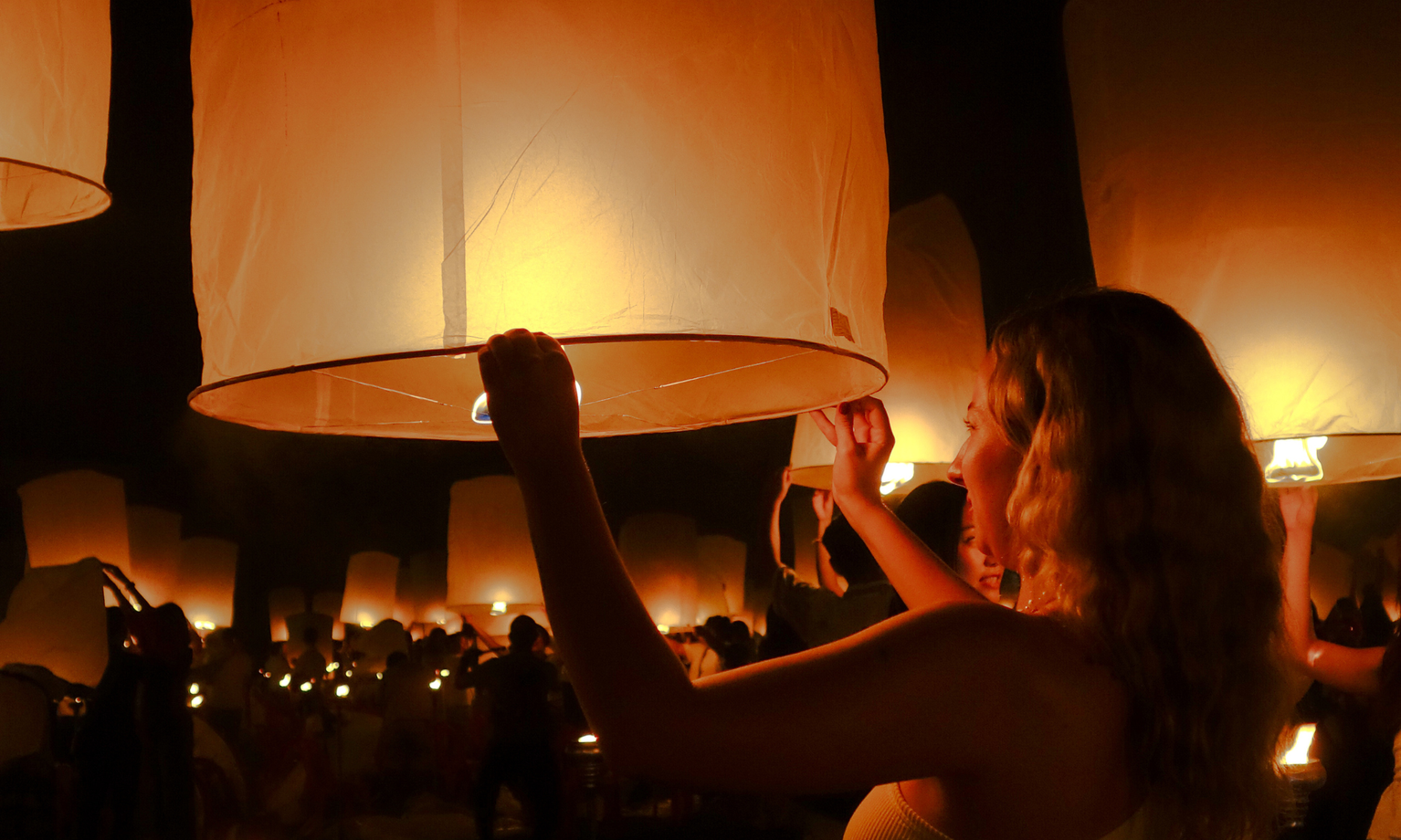 Woman holding up a lantern at night in Thailand surrounded by dozens of other lanterns