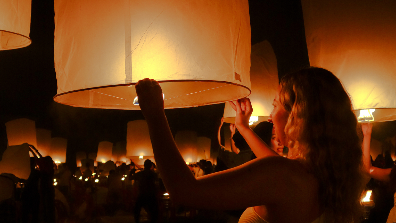 Woman holding up a lantern at night in Thailand surrounded by dozens of other lanterns