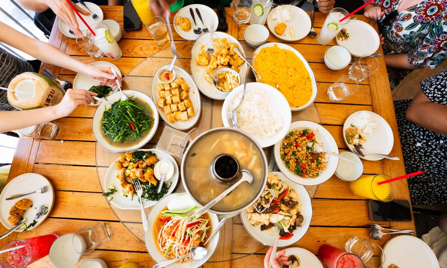 People surrounding a table full of plates of Thai food in Thailand