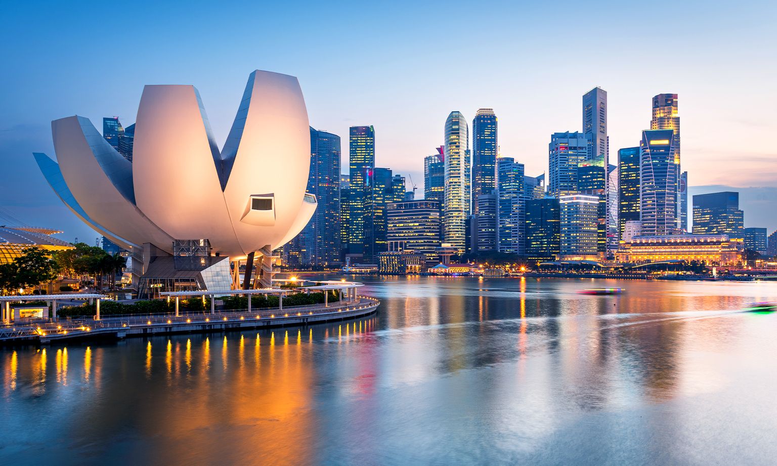 Cityscape of Singapore featuring the ArtScience Museum and illuminated skyline reflected in Marina Bay at dusk.