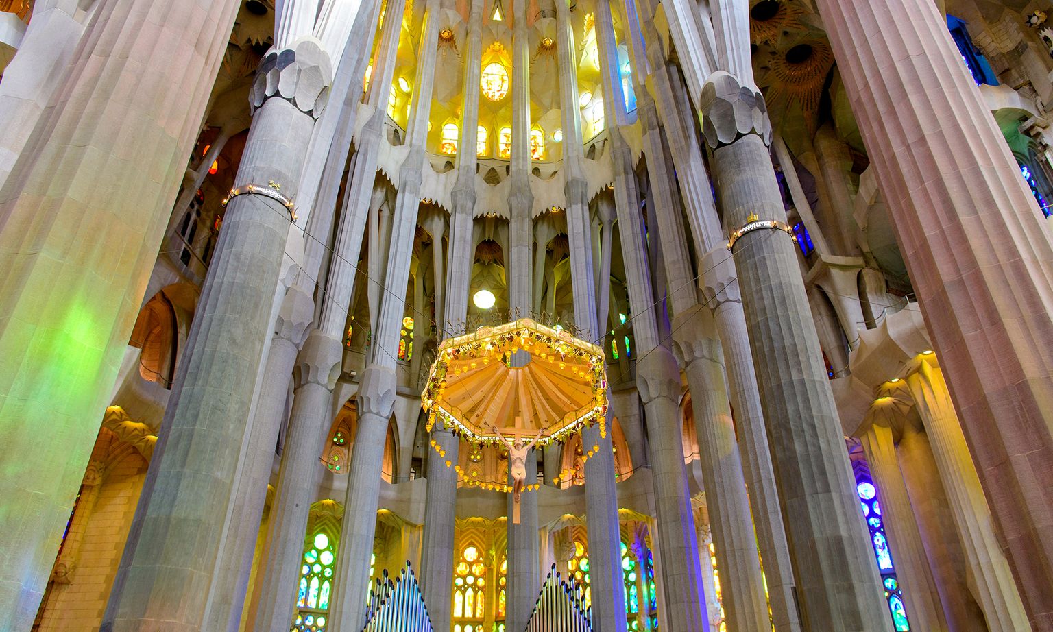Inside The Sagrada Família churches colorful windows, tall columns and vibrant chandelier.