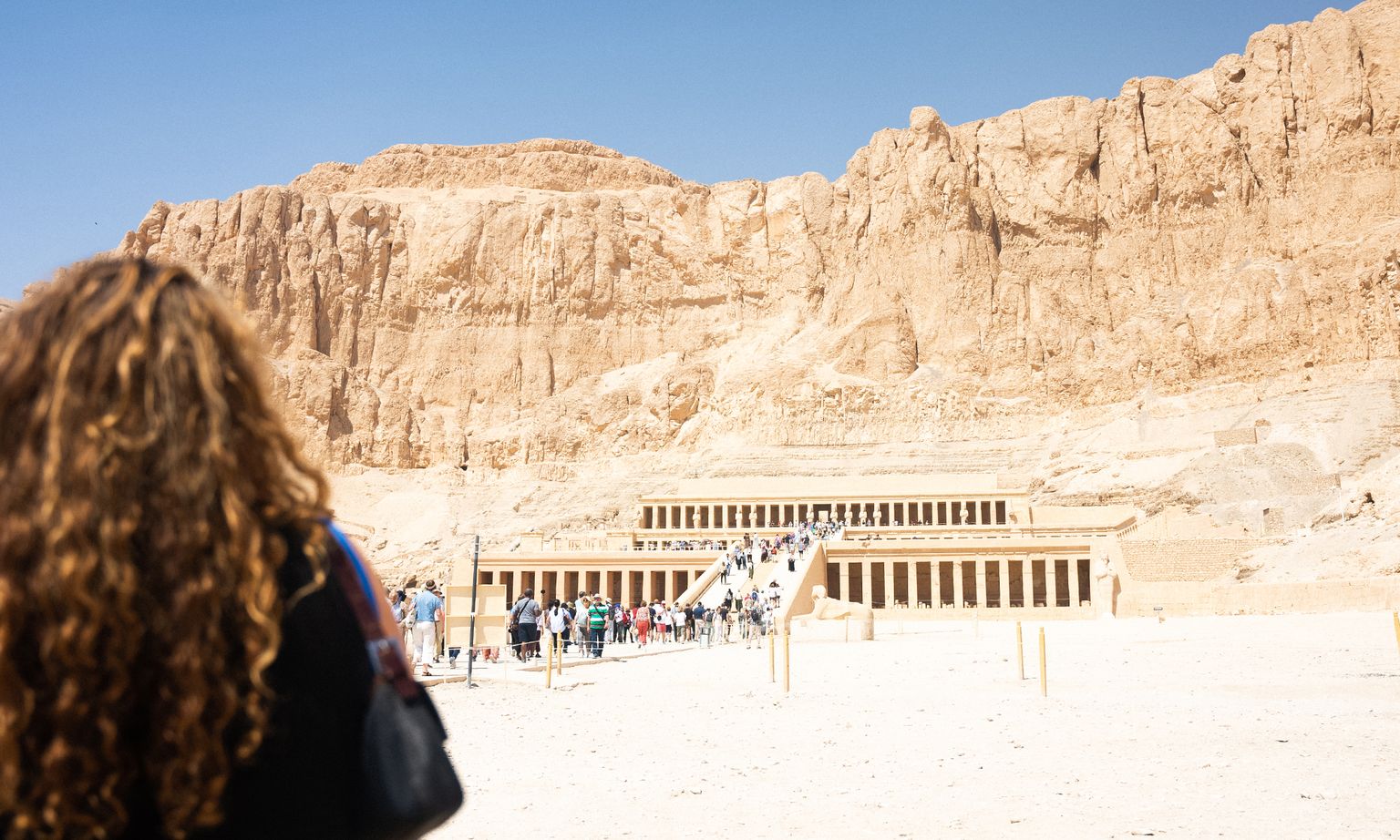 A person facing away from the camera toward the Temple of Hatshepsut on a sunny day in Egypt