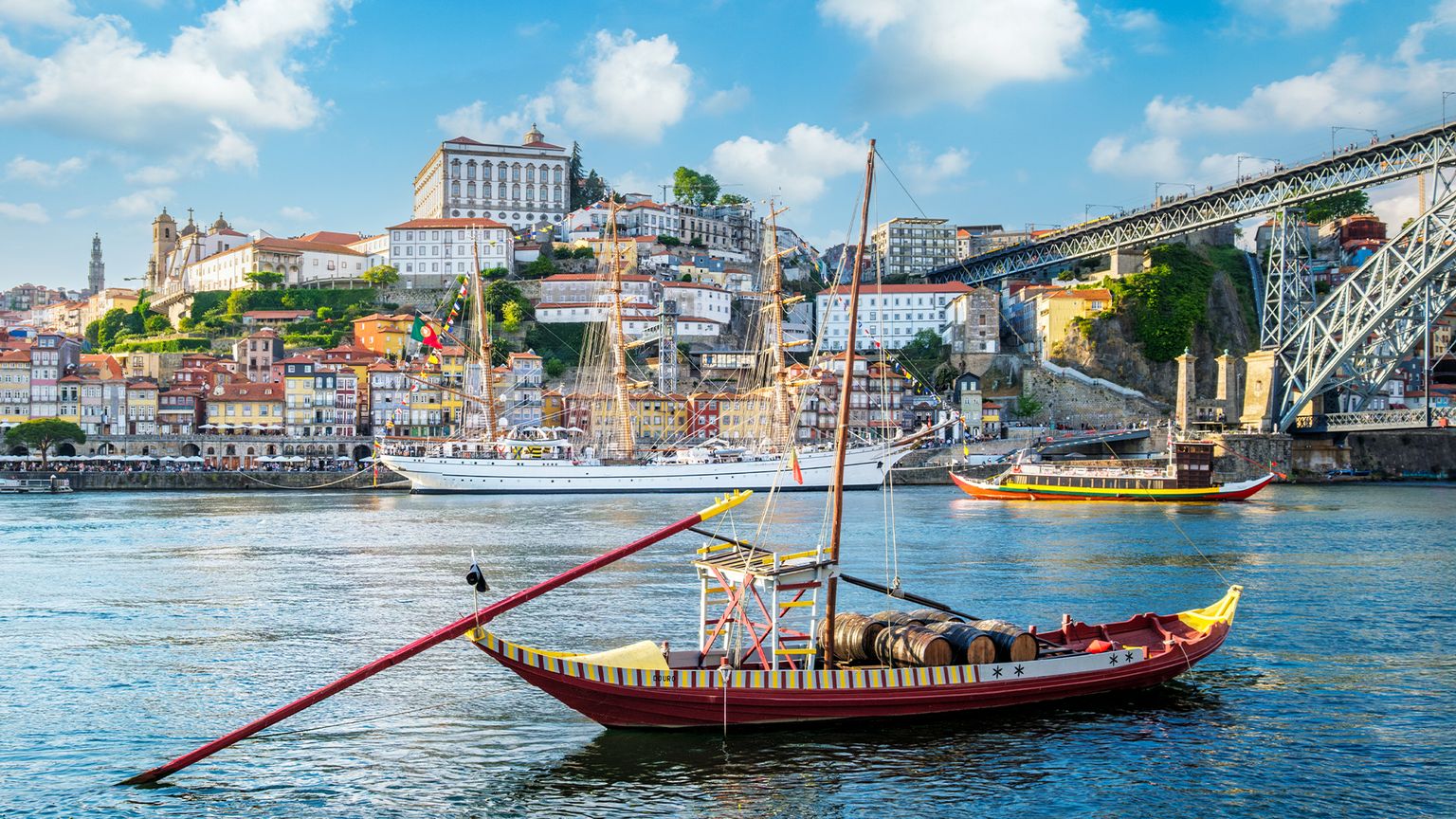 Traditional boat on the Douro River in Porto, Portugal, with a scenic view of colorful hillside buildings and the Dom Luís I Bridge.