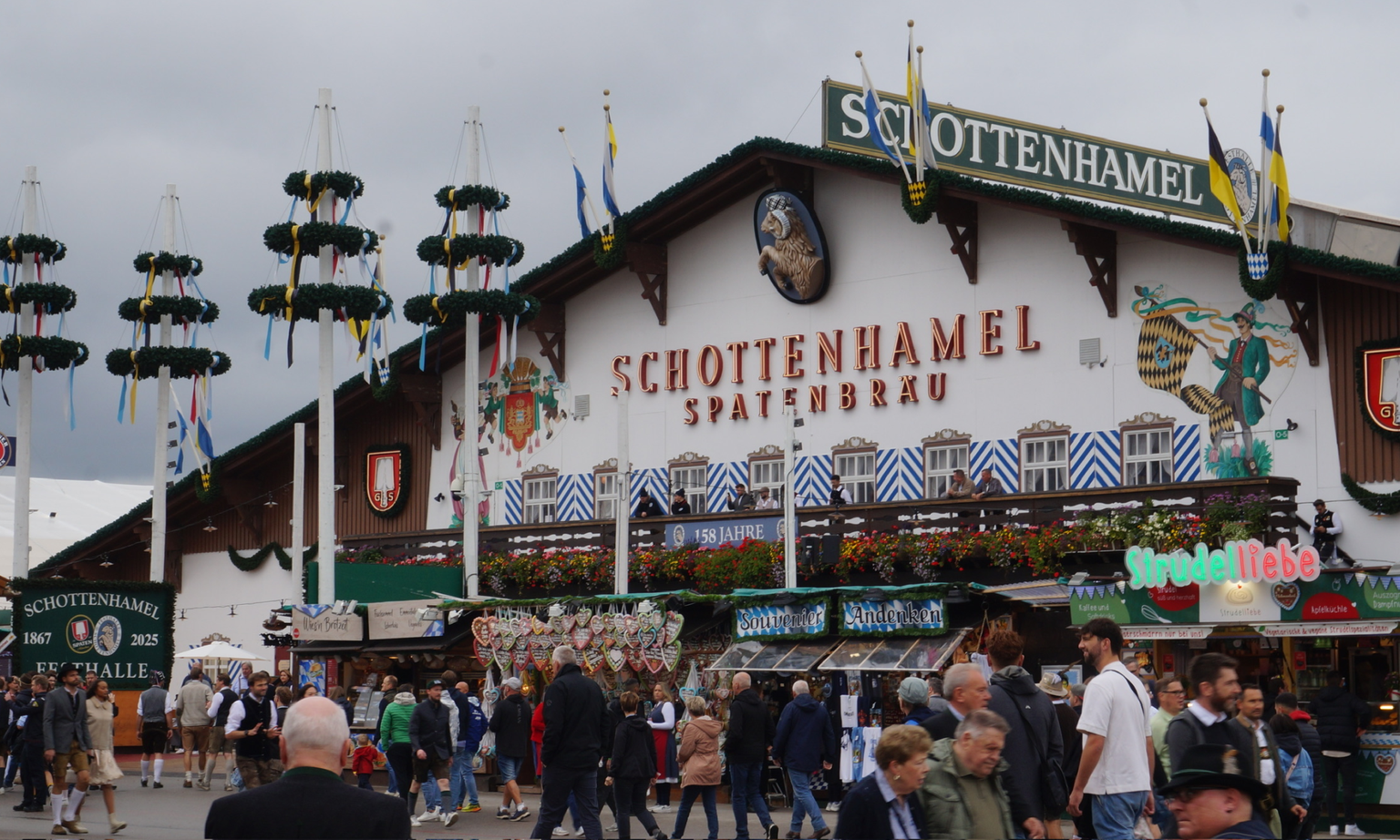 Outside of the Schottenhamel Oktoberfest tent with vendors and people walking in front.