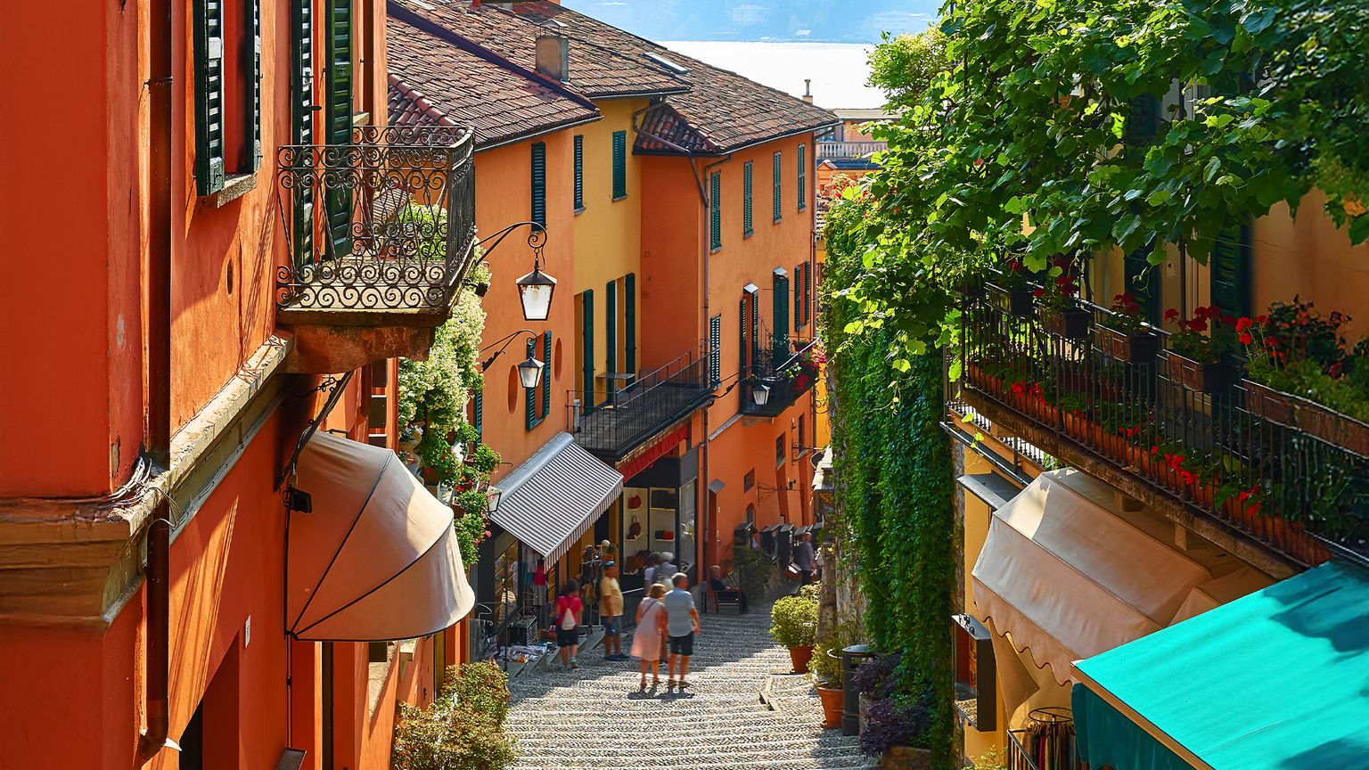 People wandering down the stairs through a street lined with colorful orange stucco buildings in Bellagio, Italy