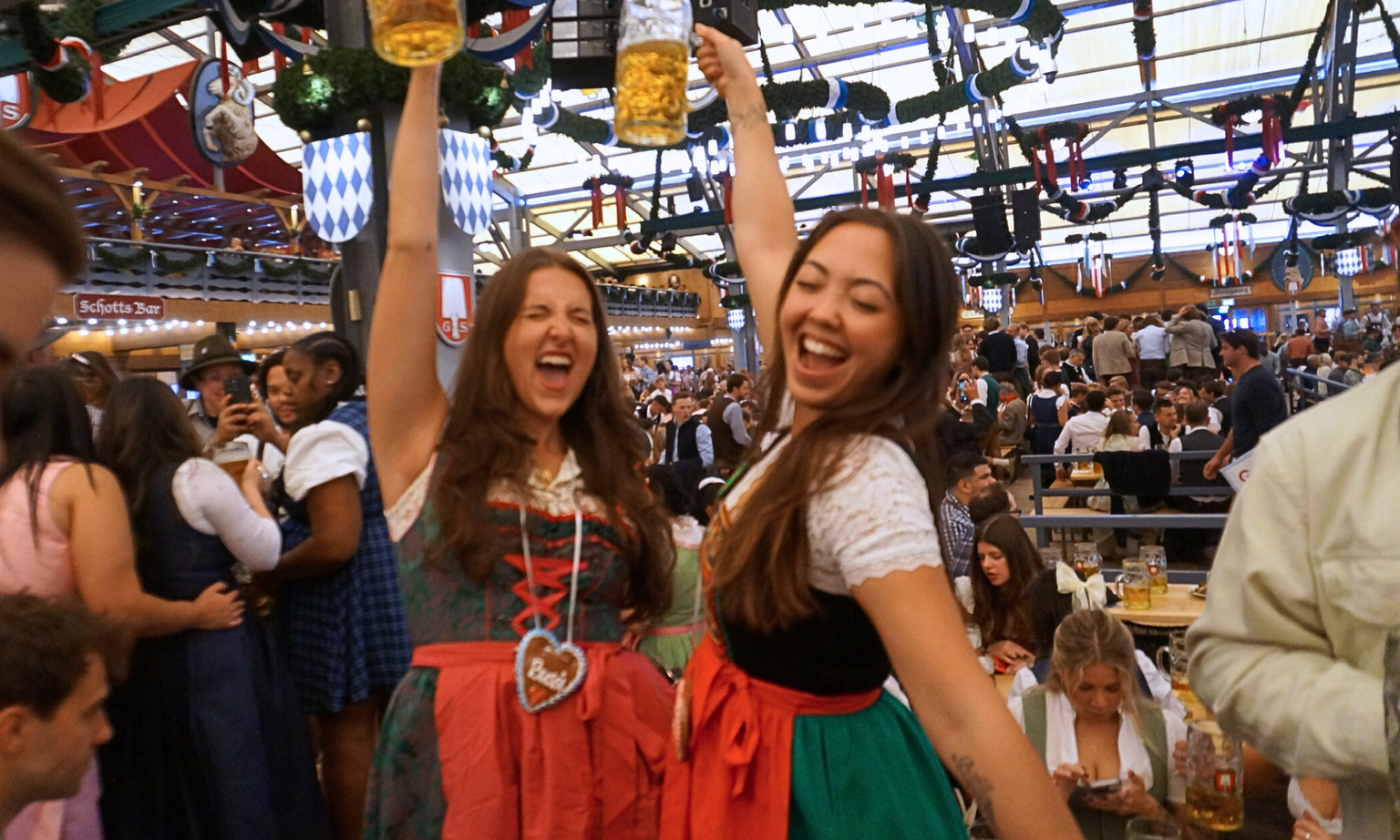 Two woman inside an Oktoberfest beer tent, raising their steins.