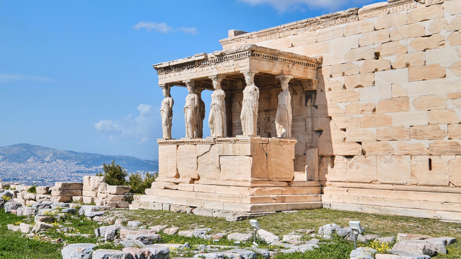 The Erechtheion with Caryatids on the Acropolis in Athens, Greece, under a clear blue sky, surrounded by scattered ancient stones.