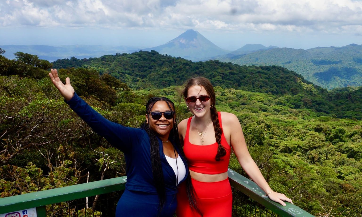 Two women posing and smiling with the Costa Rican jungle and Arenal volcano in the background