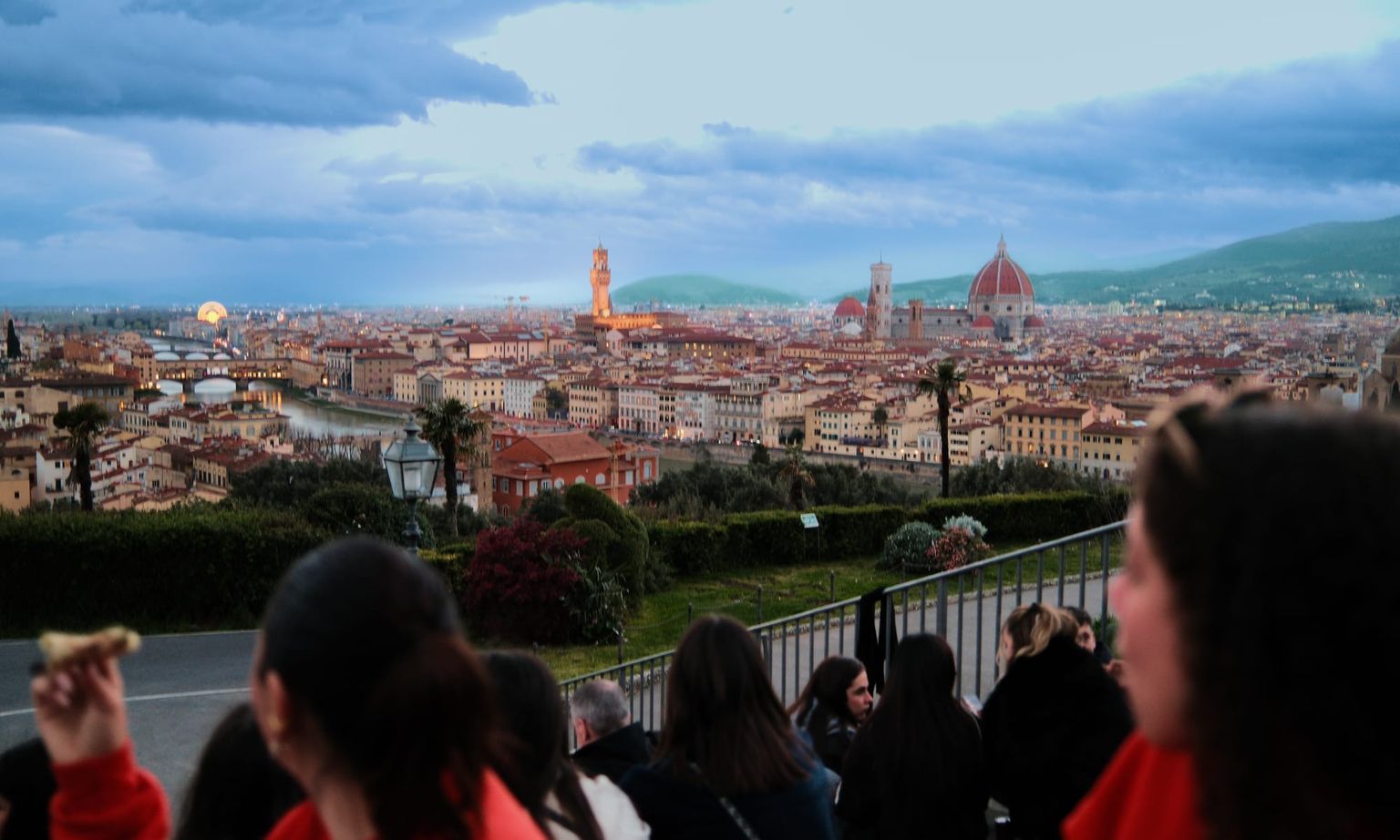 People sitting and enjoying a scenic view of Florence, featuring the Duomo and historic buildings under a cloudy sky.