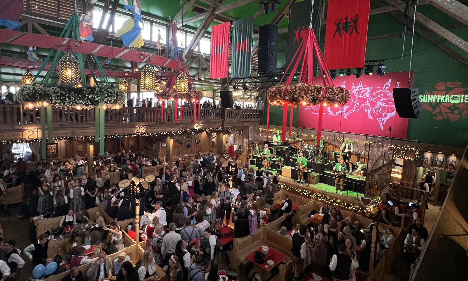 Inside the Weinzelt Oktoberfest wine tent with people standing around tables and on balconies, watching the band play in the middle.