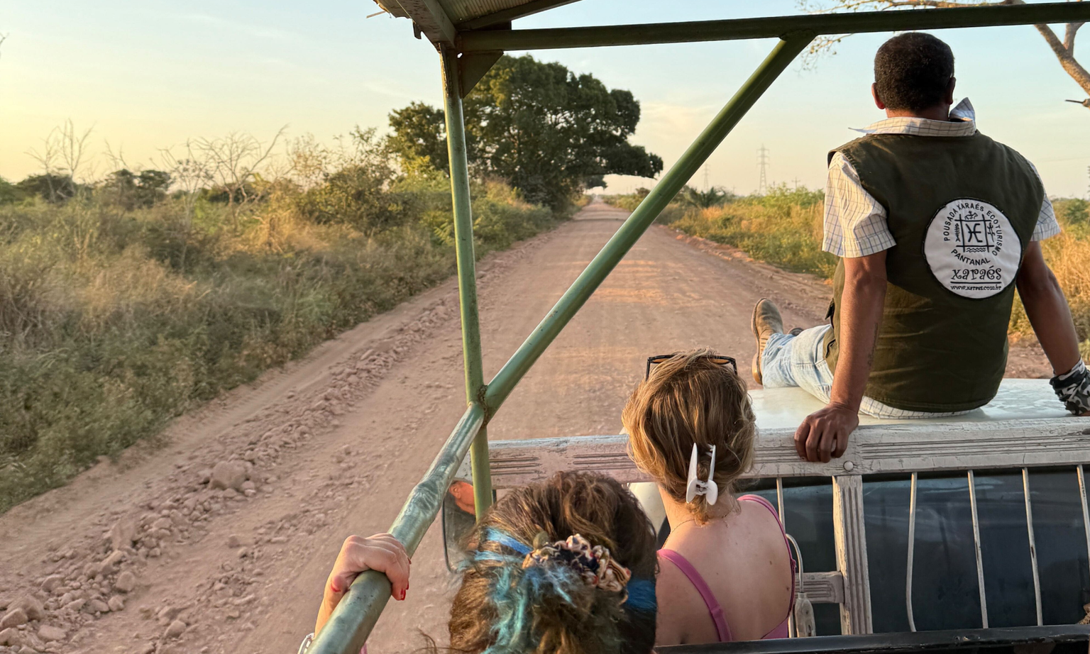 People in an open-top vehicle driving down a dirt road through Brazil's Pantanal wetlands at sunset