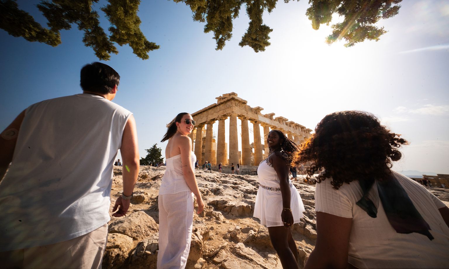 A group of people walking up a rocky hill toward the ruins of the Parthenon in Athens, Greece