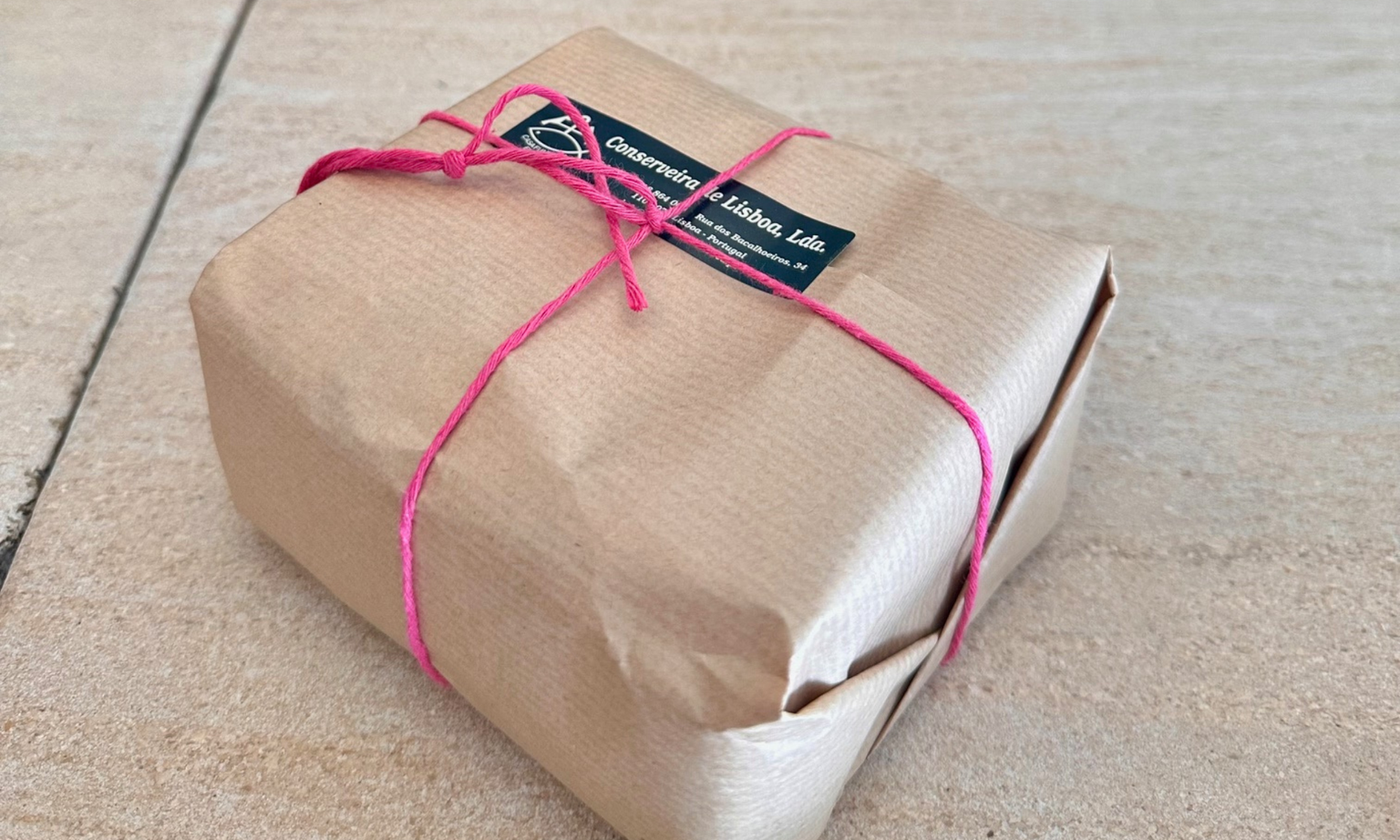 A small brown paper package tied with pink string, featuring a label with text on a light-colored surface.