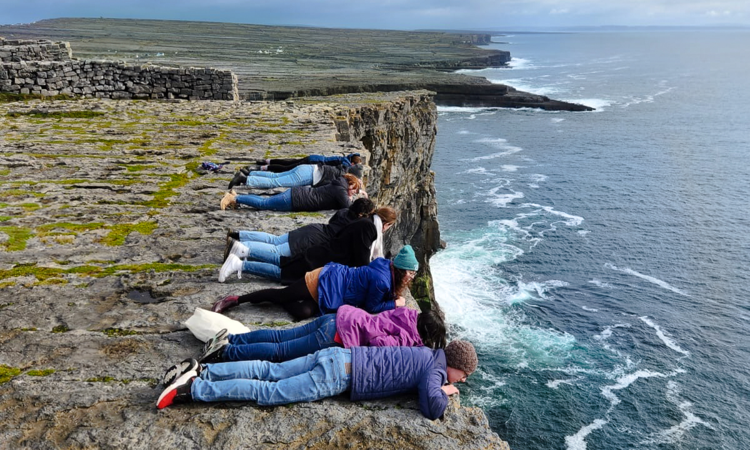 A group of people laying on the edge of a cliff with the water underneath them.