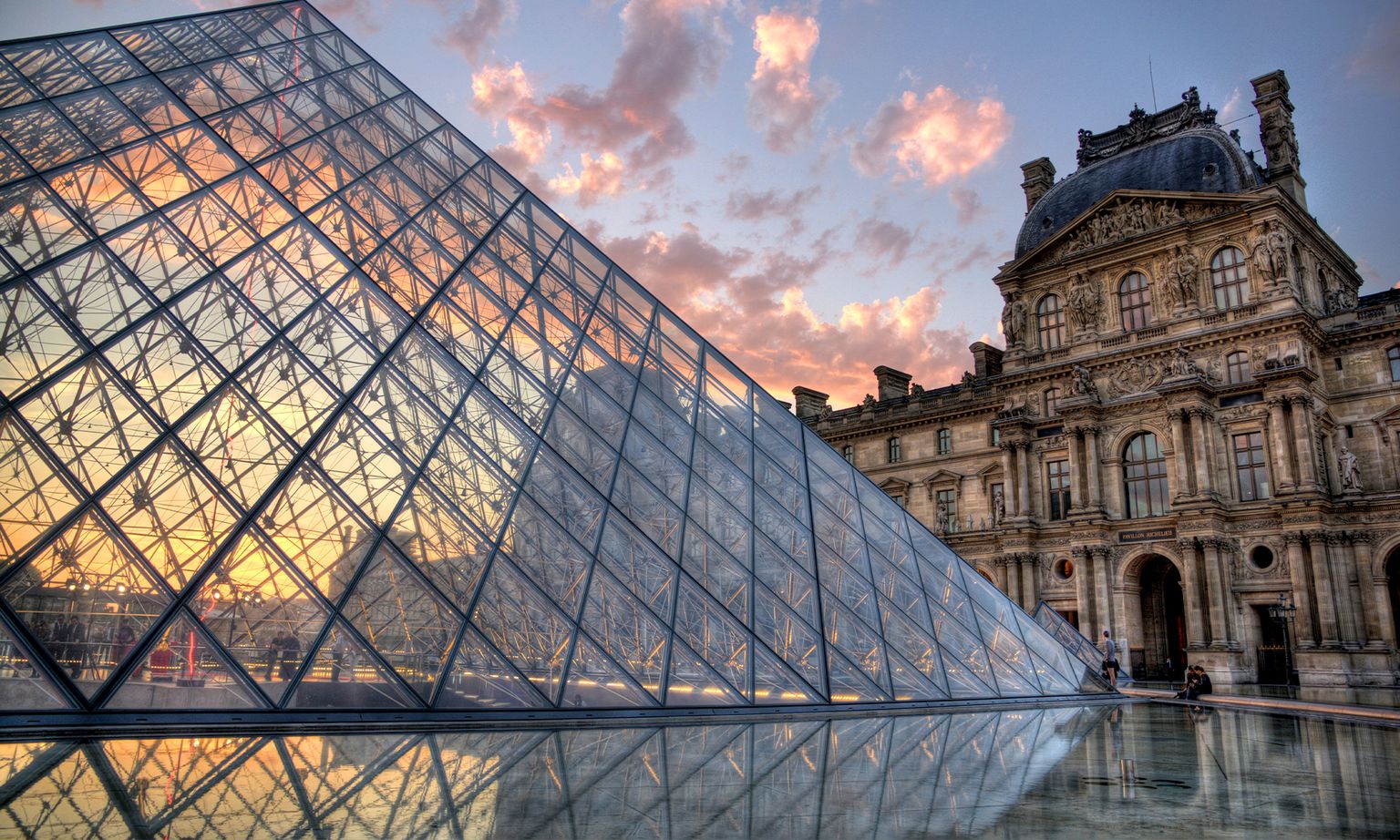 The glass pyramid entrance Louvre and a section of its ornate architecture at sunset in Paris