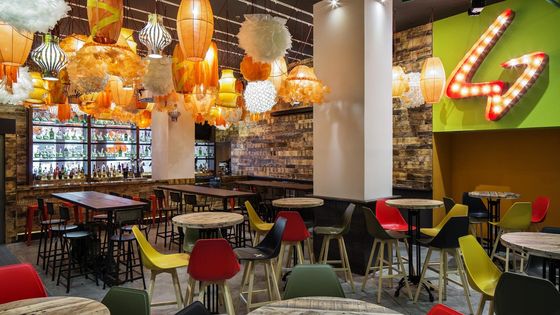 Trendy café with eclectic lanterns, colorful chairs, and rustic wooden decor. Illuminated bar shelves in the background.