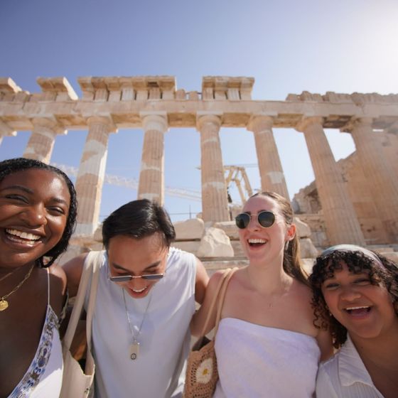 Four people smiling and posing in front of ancient ruins under a clear blue sky.