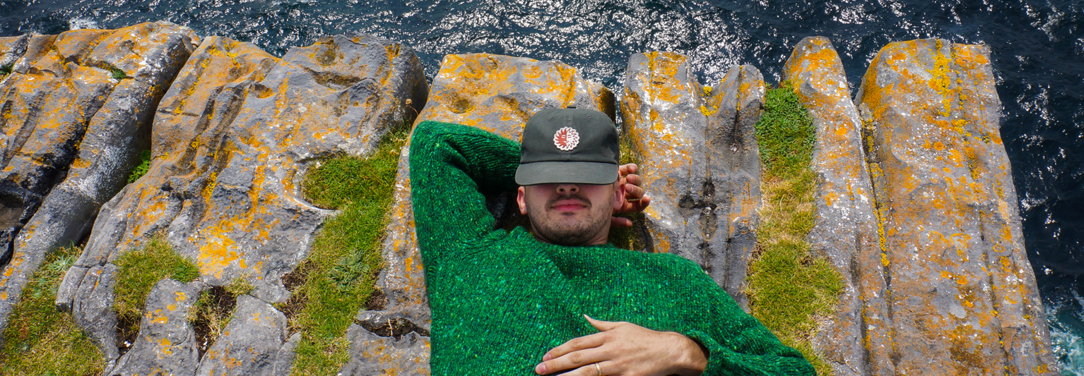 A man laying on the edge of a cliff with the water underneath him.