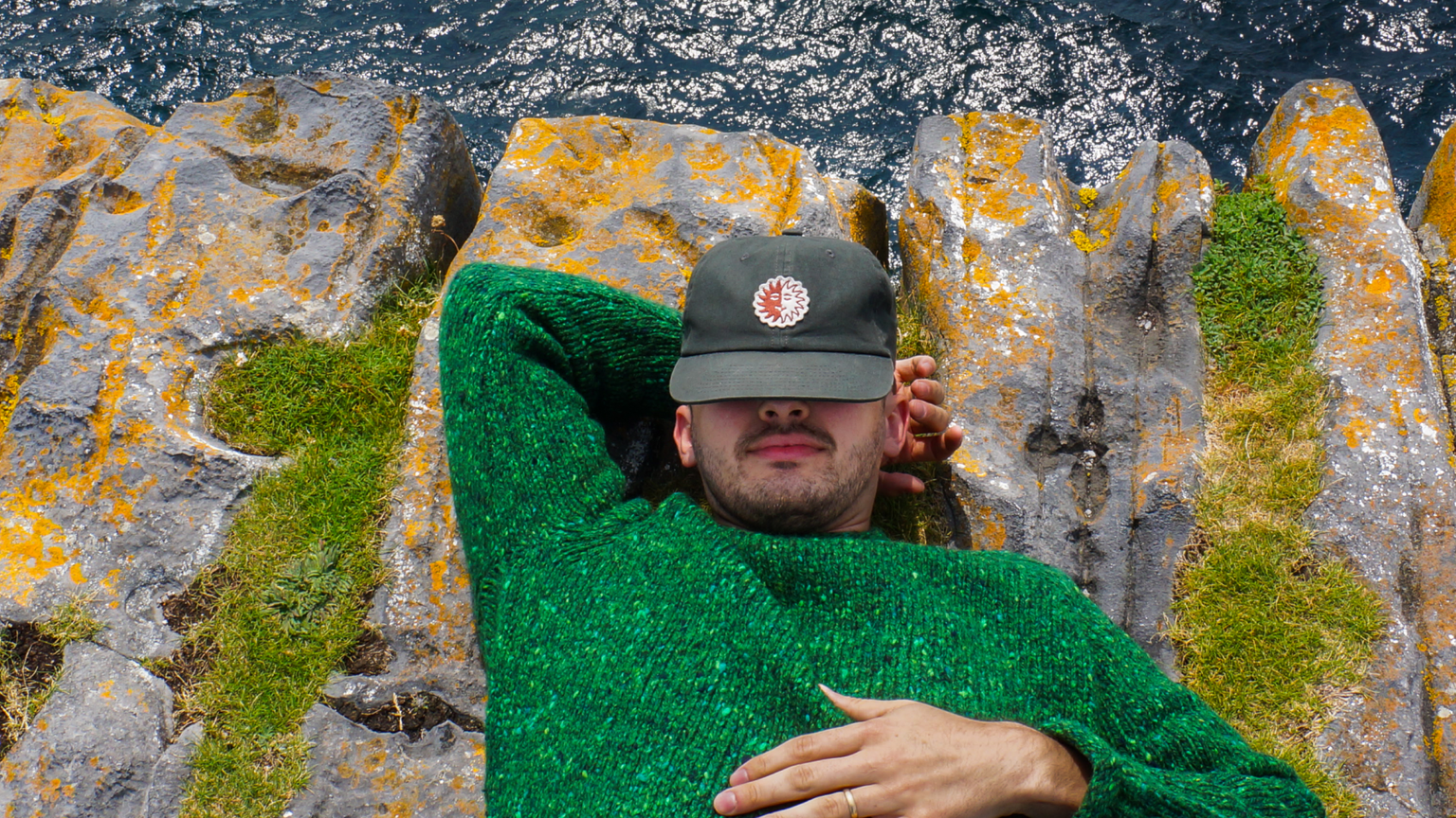 A man laying on the edge of a cliff with the water underneath him.