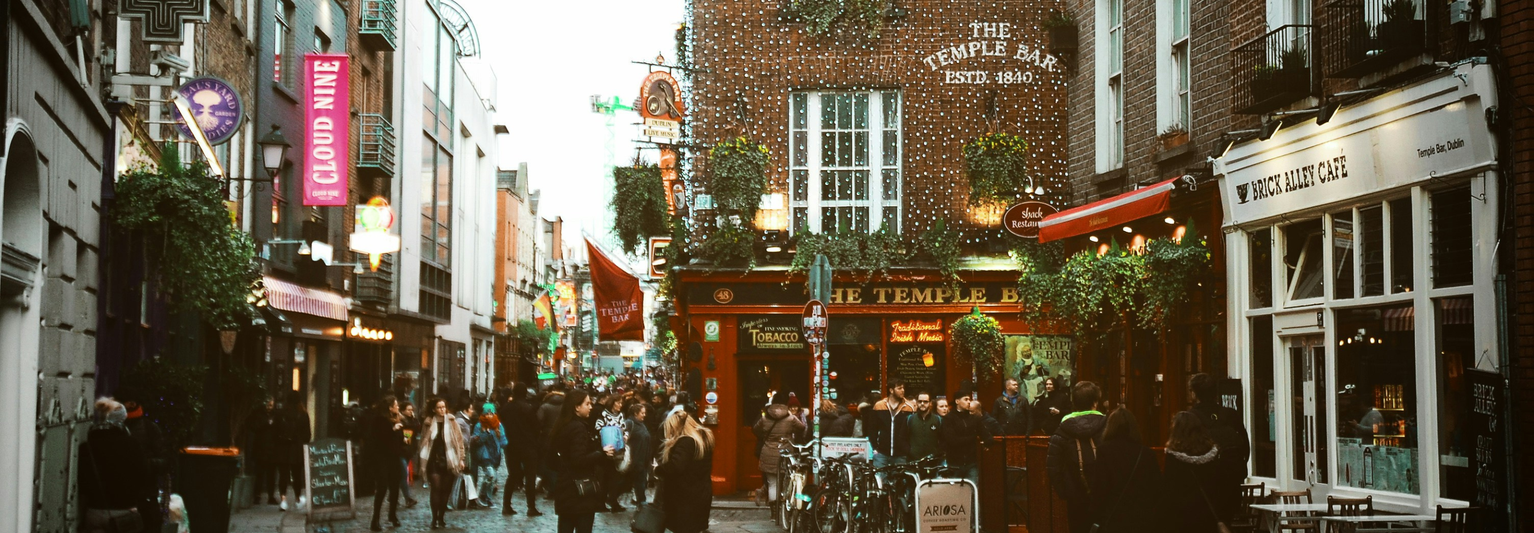 A bustling street scene at The Temple Bar in Dublin, with people walking and bicycles parked, surrounded by vibrant shops and pubs.