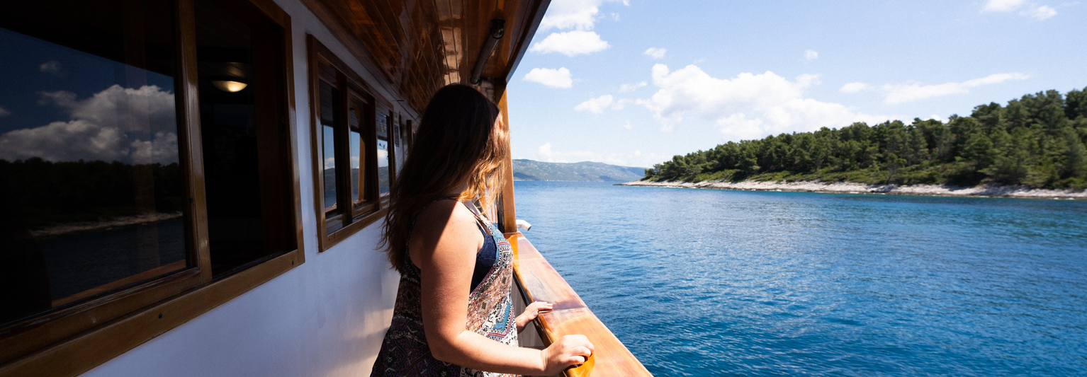 Woman on a boat gazing at the scenic view of a blue lake and forested shoreline under a clear sky.