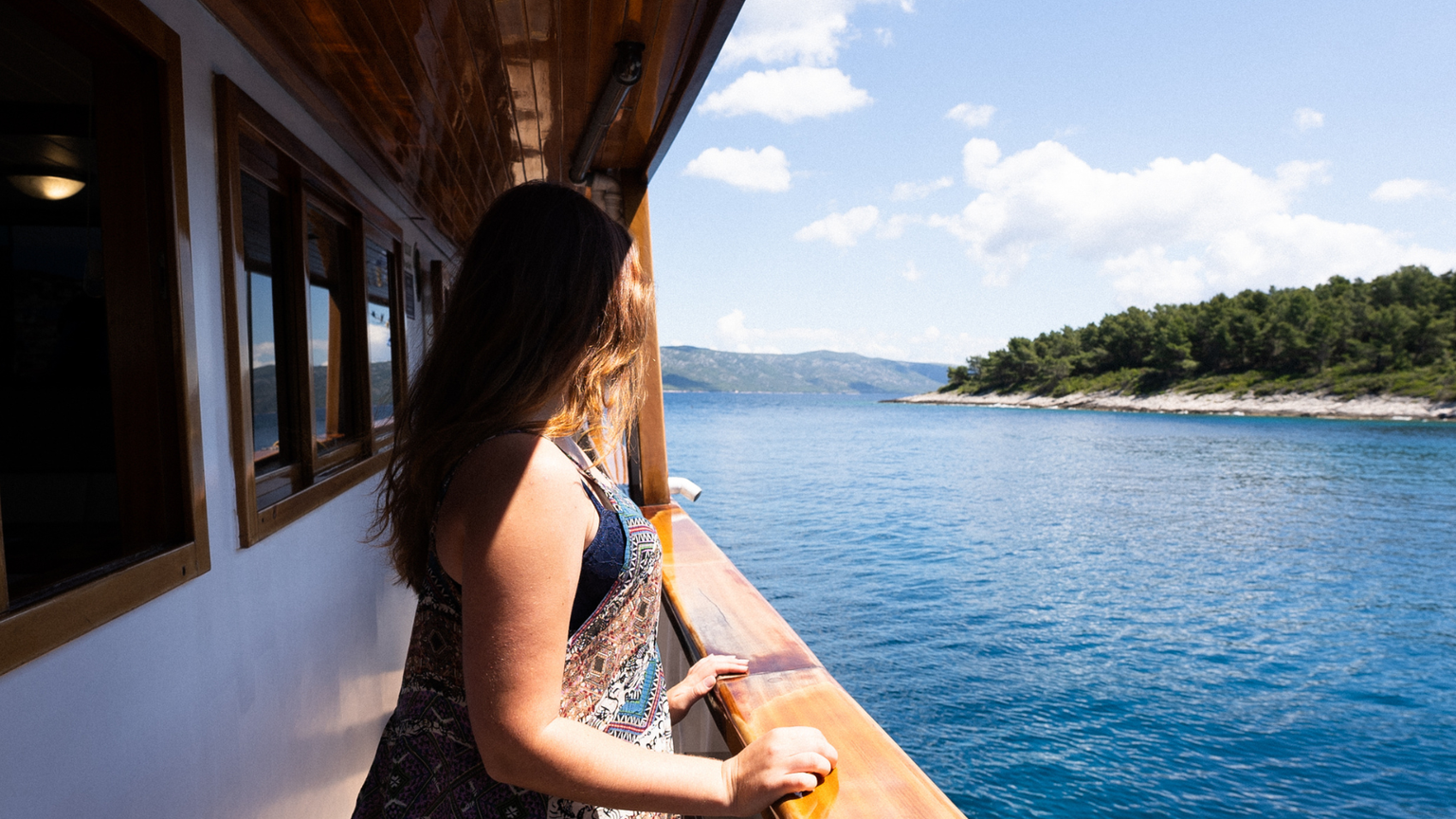 Woman on a boat gazing at the scenic view of a blue lake and forested shoreline under a clear sky.